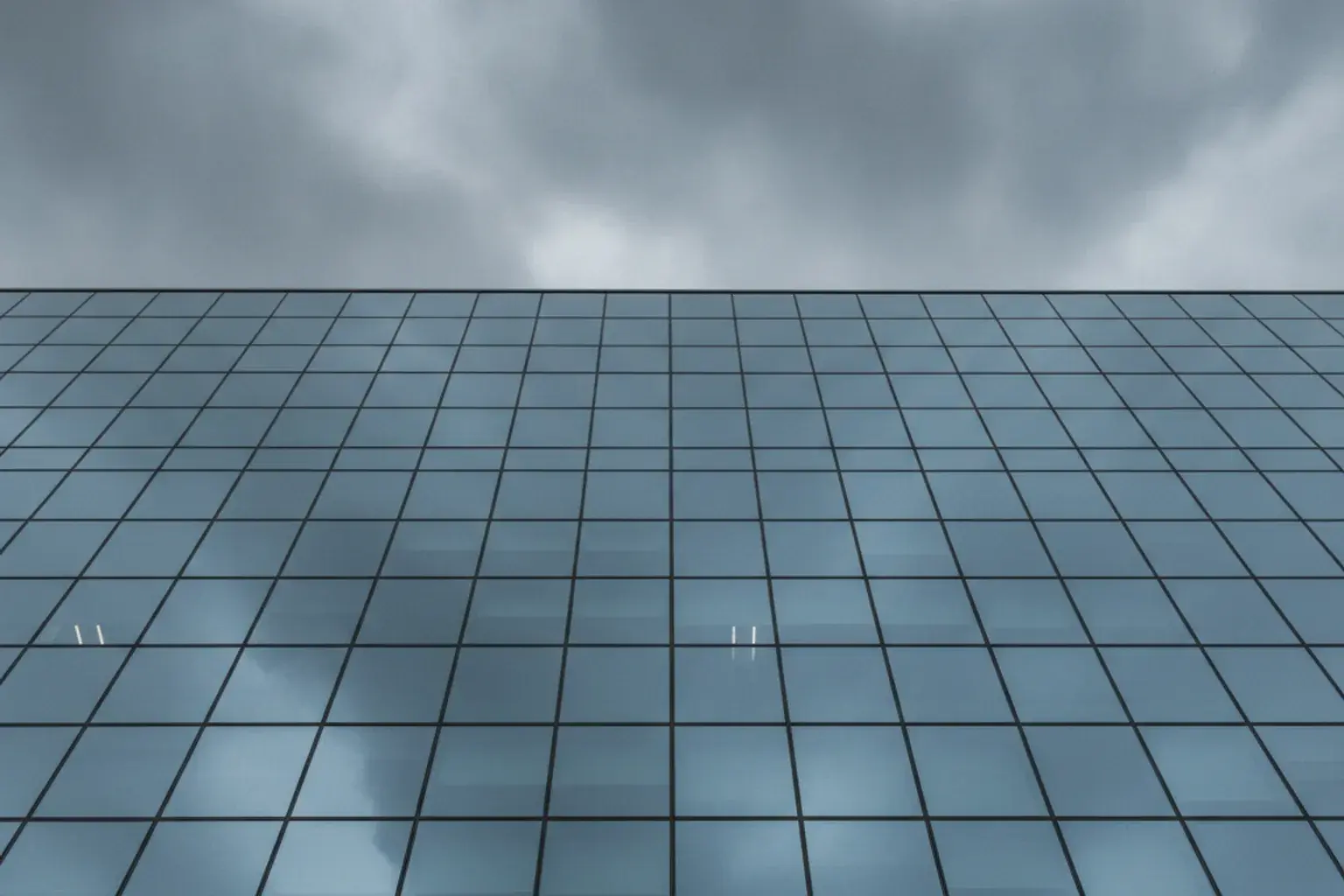 Dunkle Wolken über einer Bürohausfassade aus Glas, in der sich der Himmel spiegelt