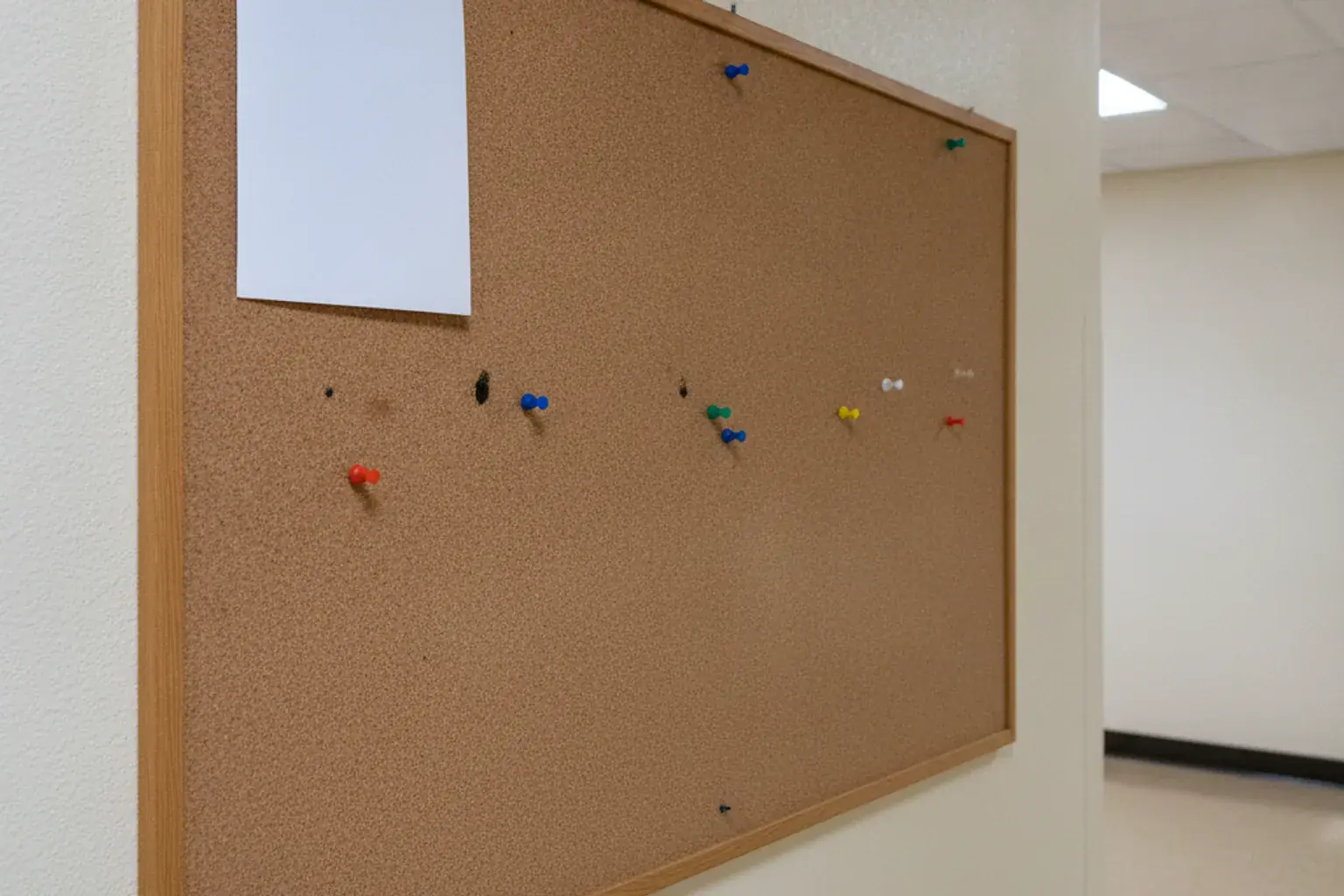 Eine leere Pinnwand mit einigen Reißzwecken und einem einzelnen unbeschrifteten Blatt Papier in einem Flur
