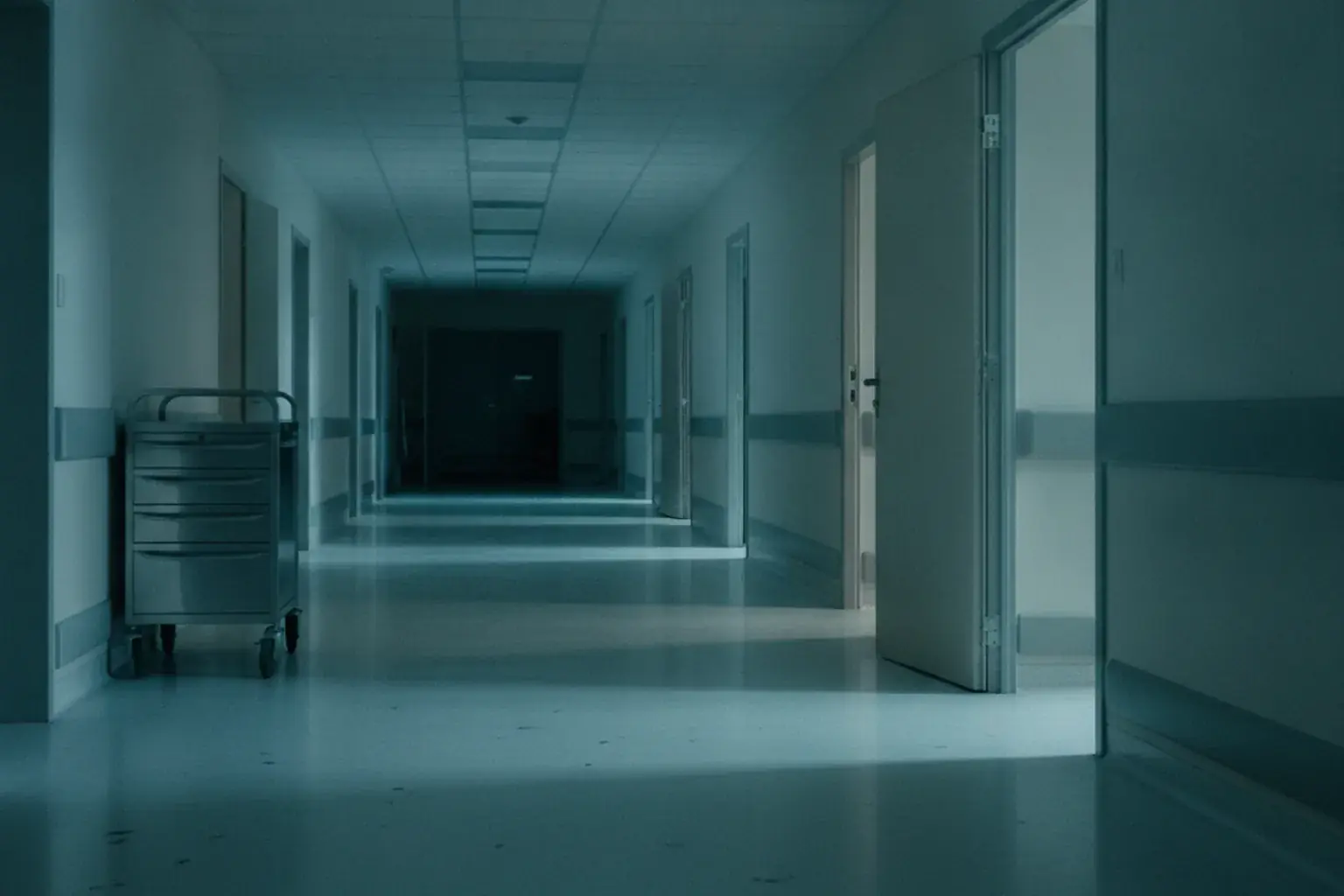 Ein leerer Krankenhausflur mit einem abgestellten Pflegewagen und einer geöffneten Zimmertür
