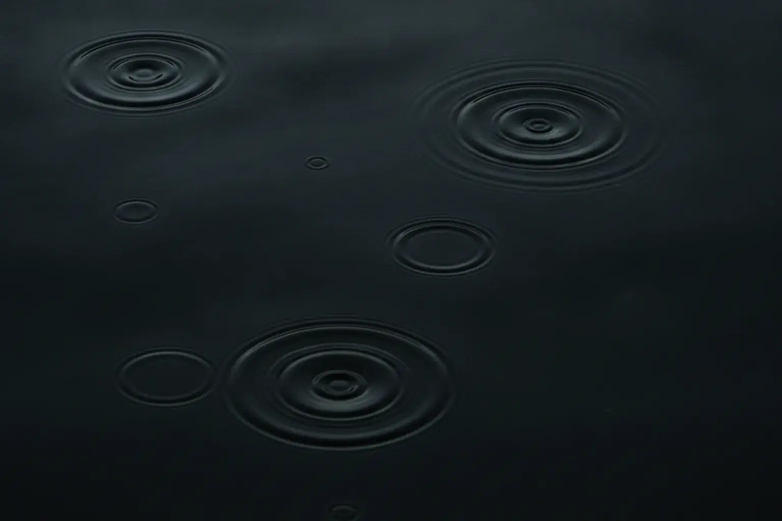 Wasseroberfläche mit unterschiedlich starken konzentrischen Ringen nach mehreren Tropfen