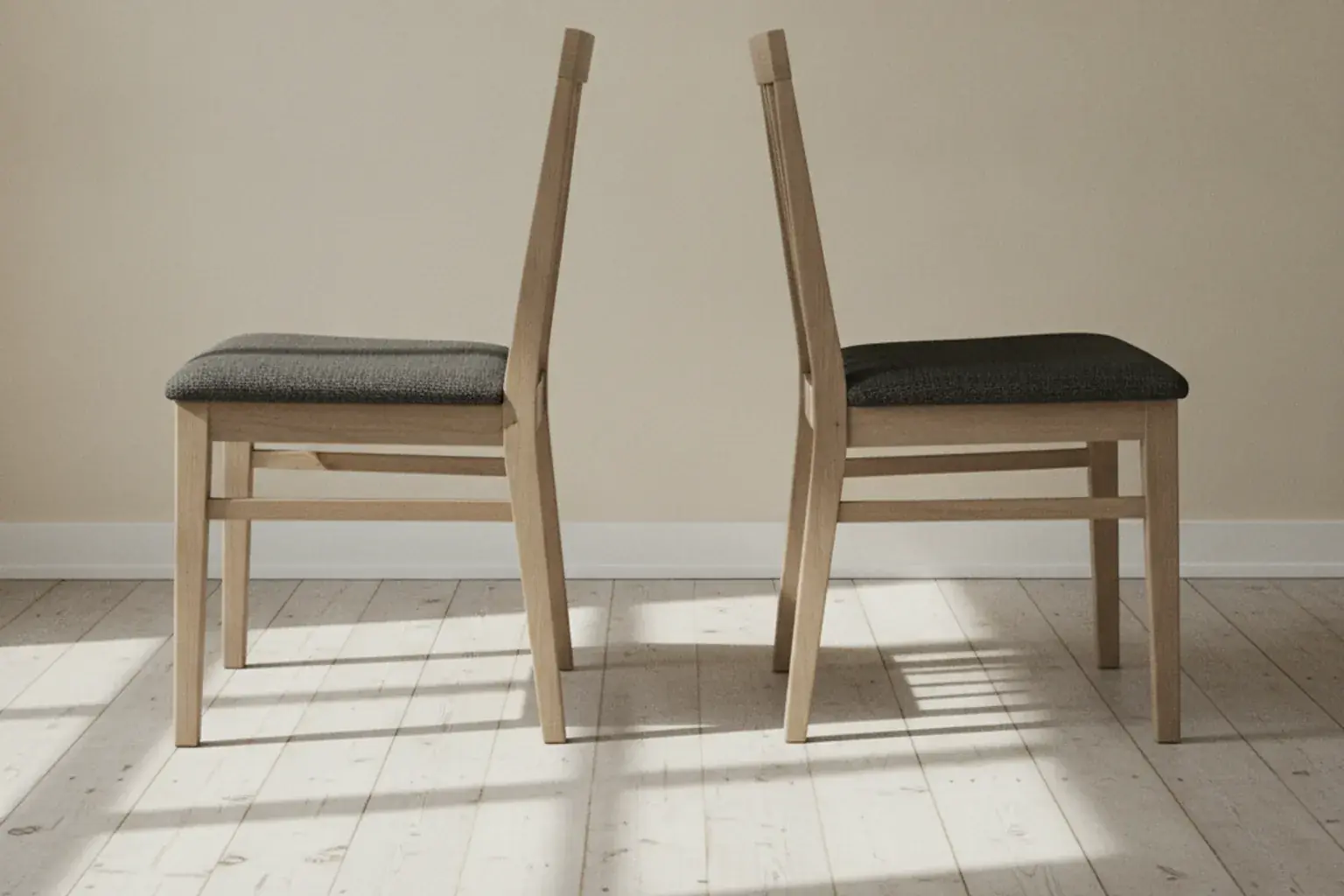 Zwei gleiche Holzstühle mit dunklen Sitzflächen stehen Rücken an Rücken in einem leeren Raum mit heller Wand